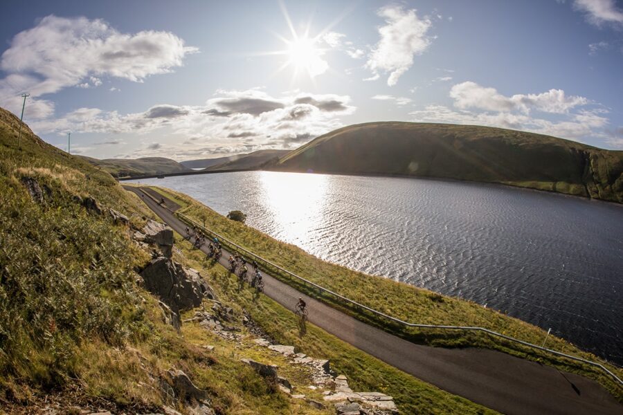 Road cyclists by Megget Reservoir in sunshine.
